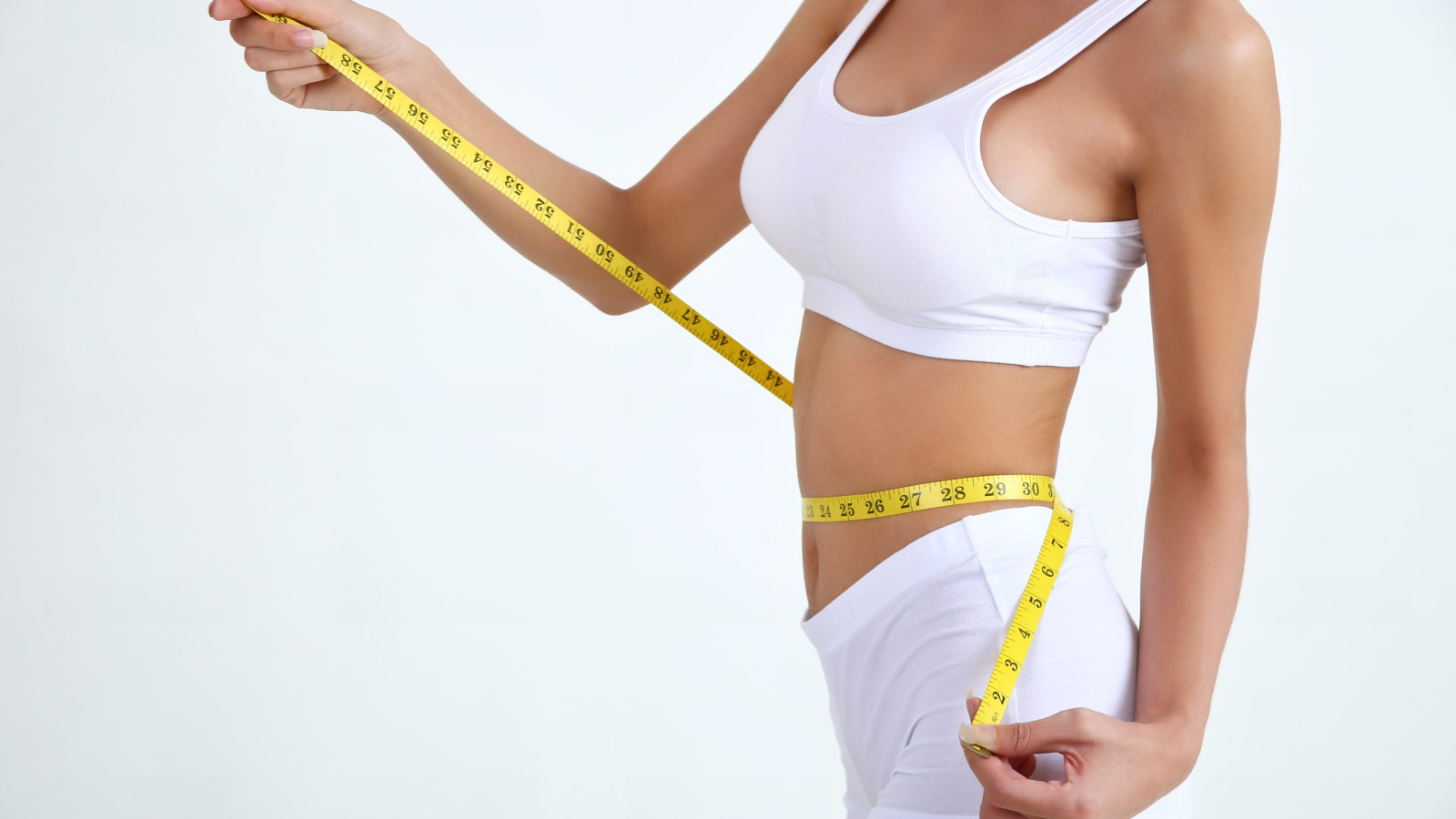 Close up slimming female with beautiful body and measuring her waistline  with measure tape on white background and copy space